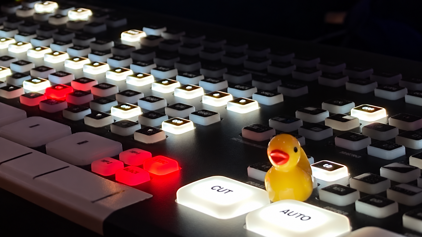 Illuminated video production switcher with a small rubber duck beside the CUT and AUTO buttons